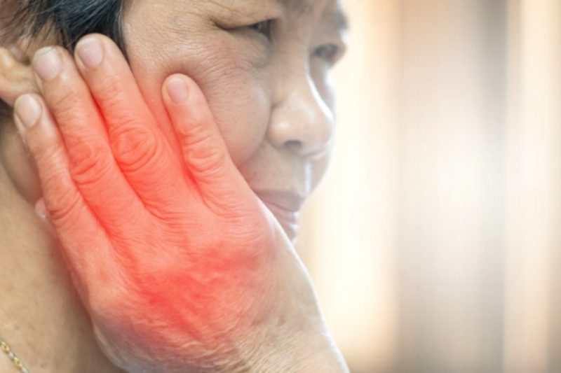 Person holding cheek in pain, redness visible.